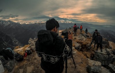 Hiker atop ledge taking picture of group with SLR camera