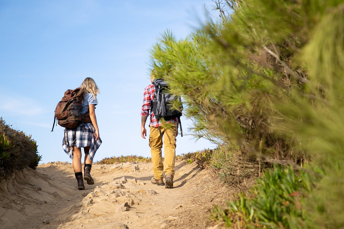 Two hikers walking uphill with backpacks on a trail.