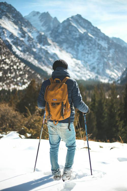 Hiker with a yellow backpack using trekking poles while standing in a snowy alpine landscape