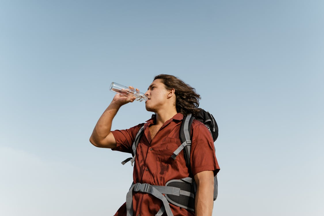 A backpacker pauses under a clear sky, drinking water from a bottle during a hike.