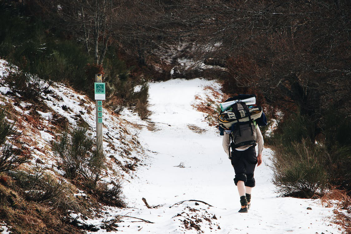 Hiker carrying a fully loaded backpack while walking along a snowy mountain trail