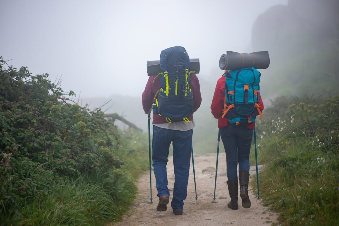 Two hikers carrying backpacks and trekking poles walk along a foggy trail, showing the benefits of a comfortable hiking backpack for long-distance hikes.
