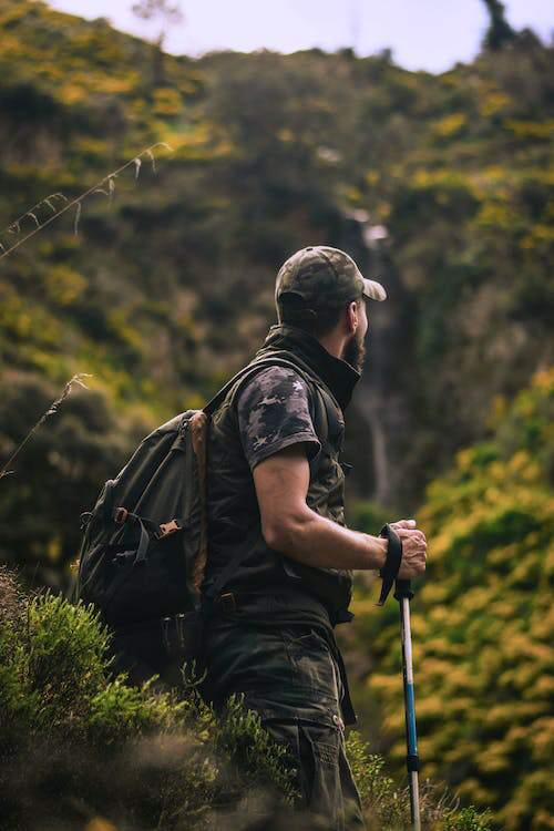 Male hiker wearing a trekking backpack and holding a hiking pole while navigating a forest trail