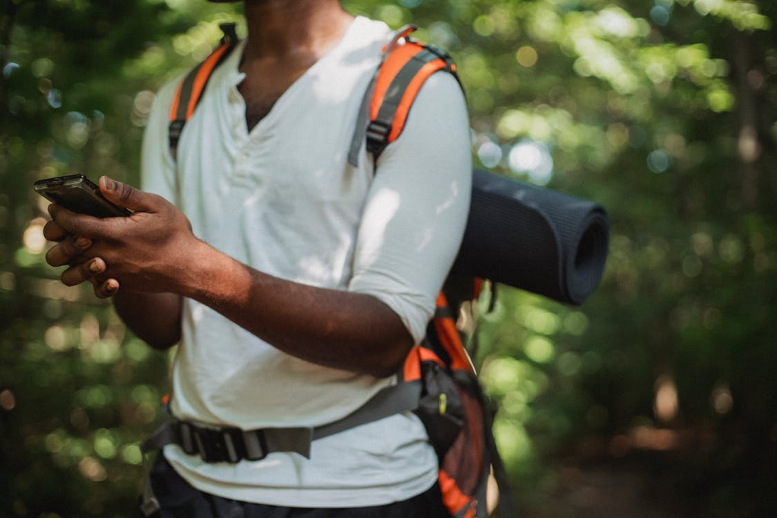 A hiker with a backpack checks a smartphone while standing on a forest trail.