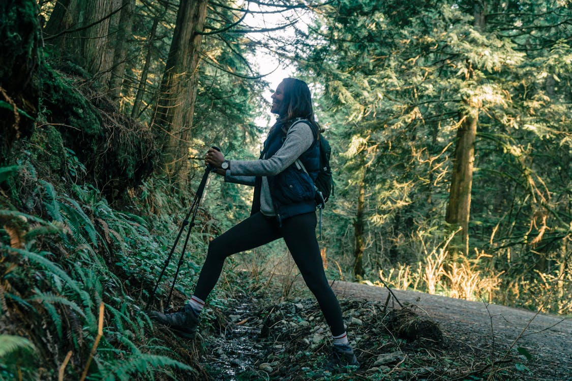 Hiker using trekking poles climbs a forest trail while wearing a backpack.