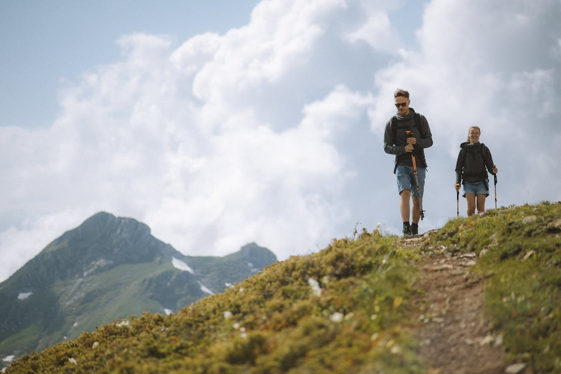 Two hikers walking downhill on a mountain trail.