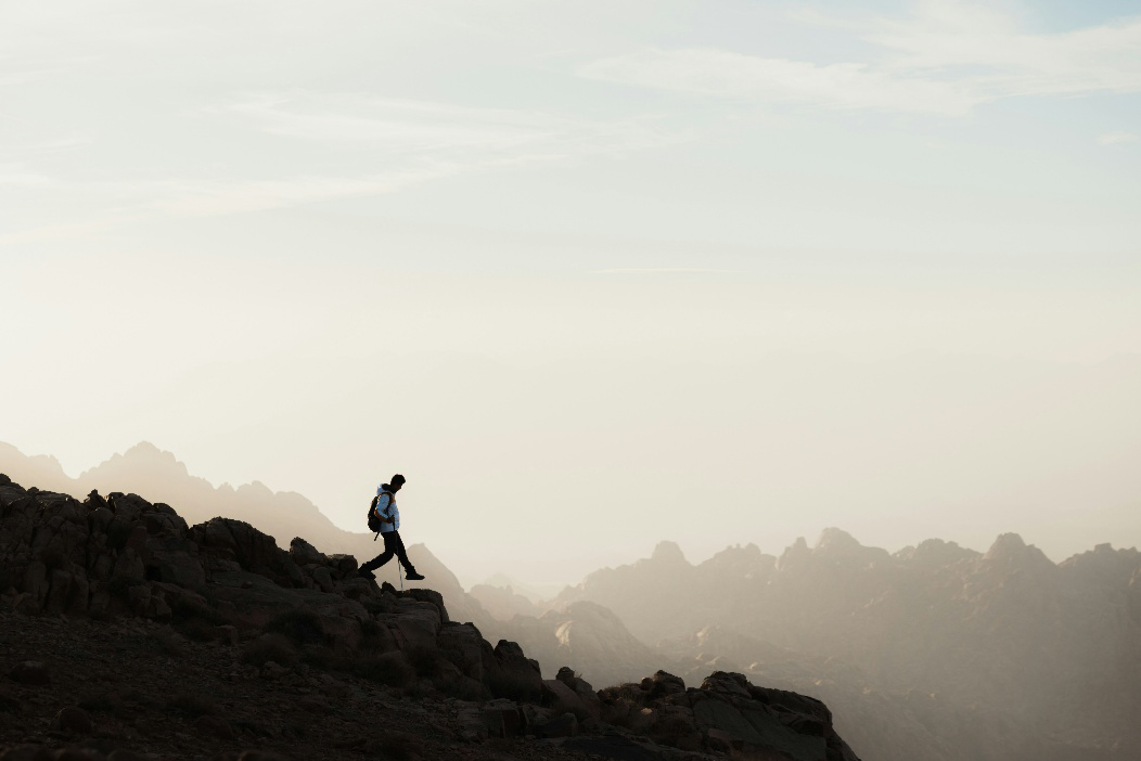 Solo hiker wearing a backpack while traversing a rocky mountain landscape during an outdoor trek.