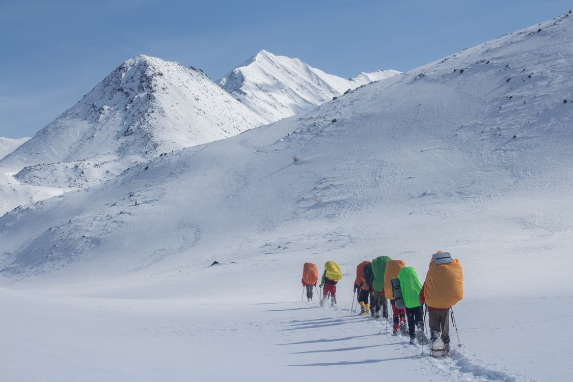Line of snowshoers with colorful waterproof backpack covers trekking across a snowy mountain range